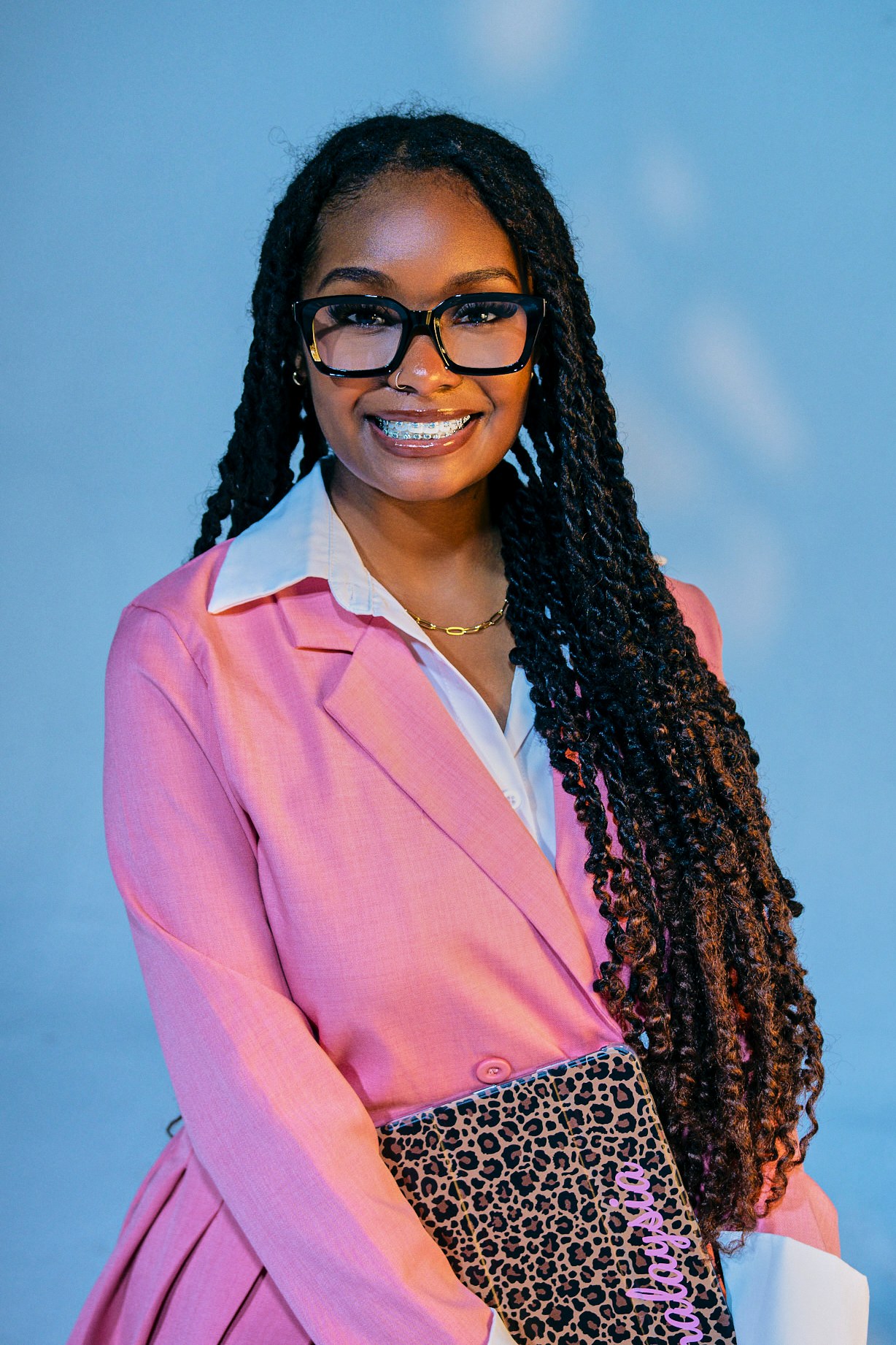 Portrait in a pink blazer and glasses, holding a patterned folder.